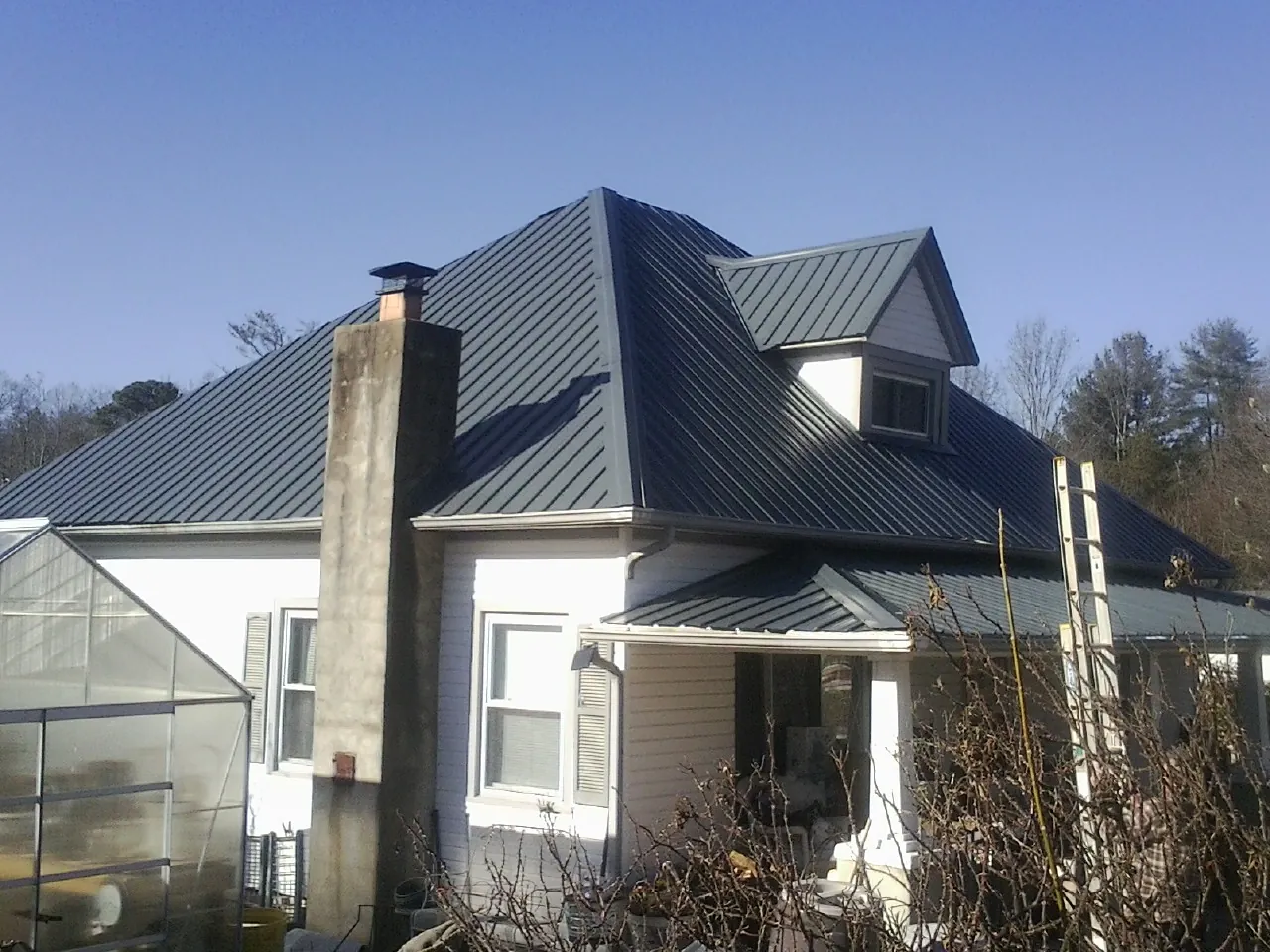 Dark blue standing seam metal roof on a white farmhouse with dormer — Slate & Tile Roof Repair by Roofing Brothers in Rougemont