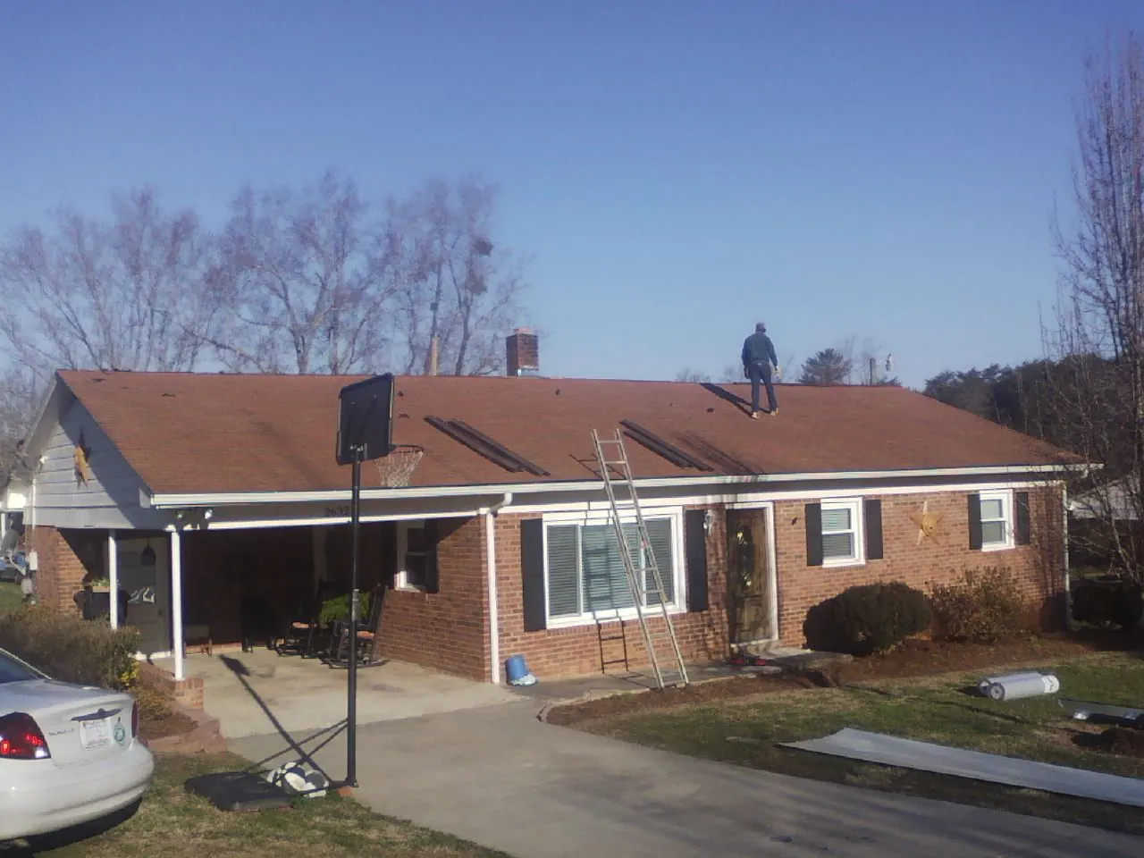 Roofer stripping a shingle roof on a brick ranch before metal panels in Rougemont