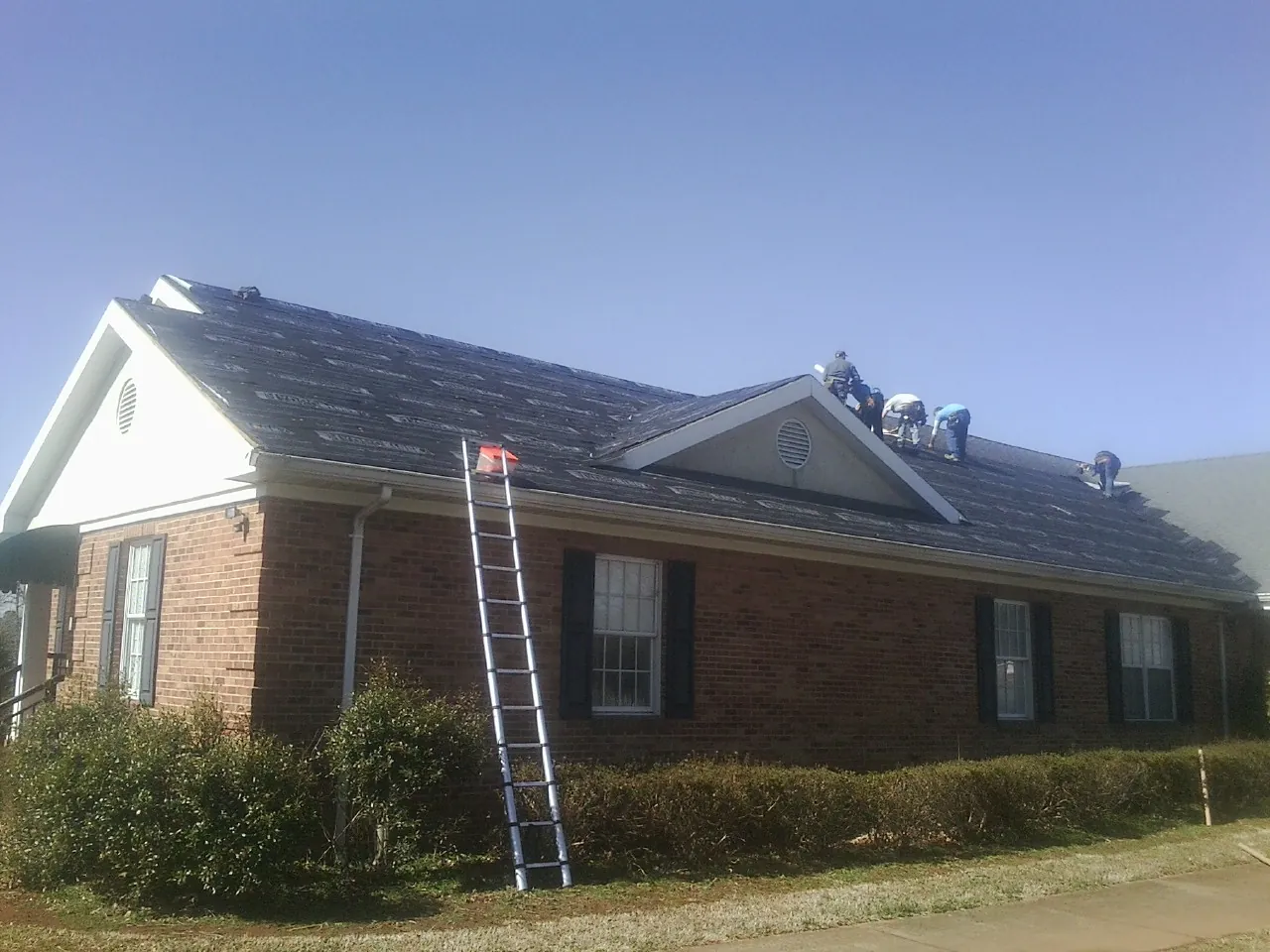Crew tearing shingles off a brick ranch roof with a ladder set — Emergency Roof Repair work by our crew in Rougemont