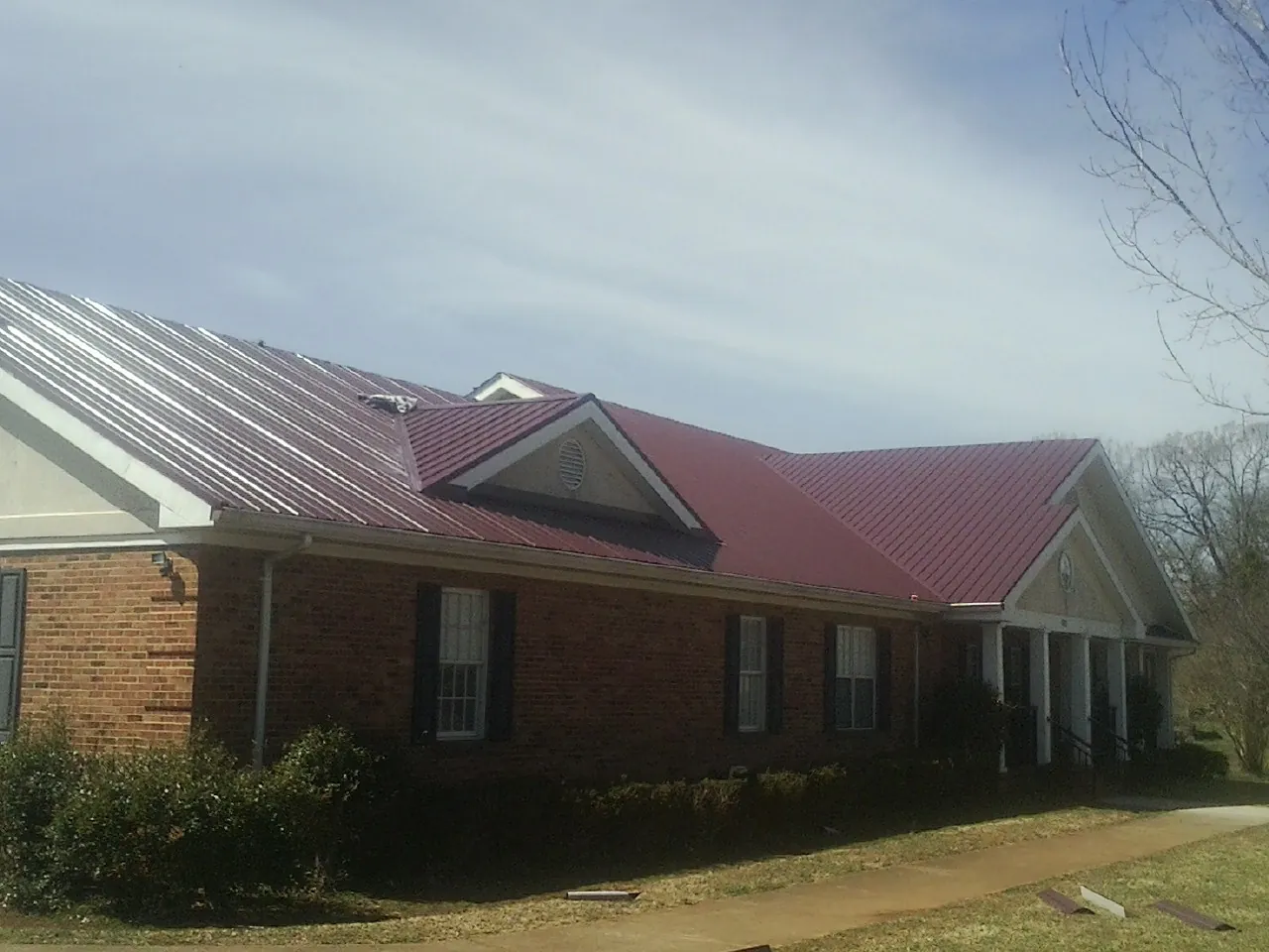 Red metal roof with gabled entries on a long brick building, from a Hail Damage Roof Repair job in Rougemont