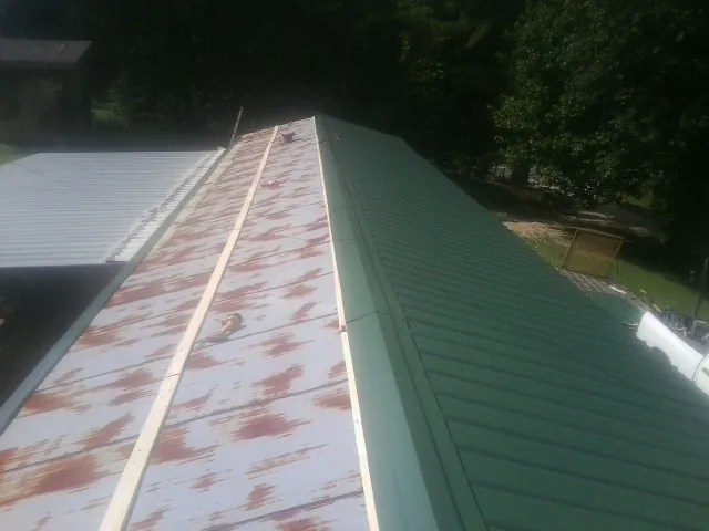 Old rusted panels beside newly installed green metal roofing — Wind Damage Roof Repair by Roofing Brothers in Rougemont