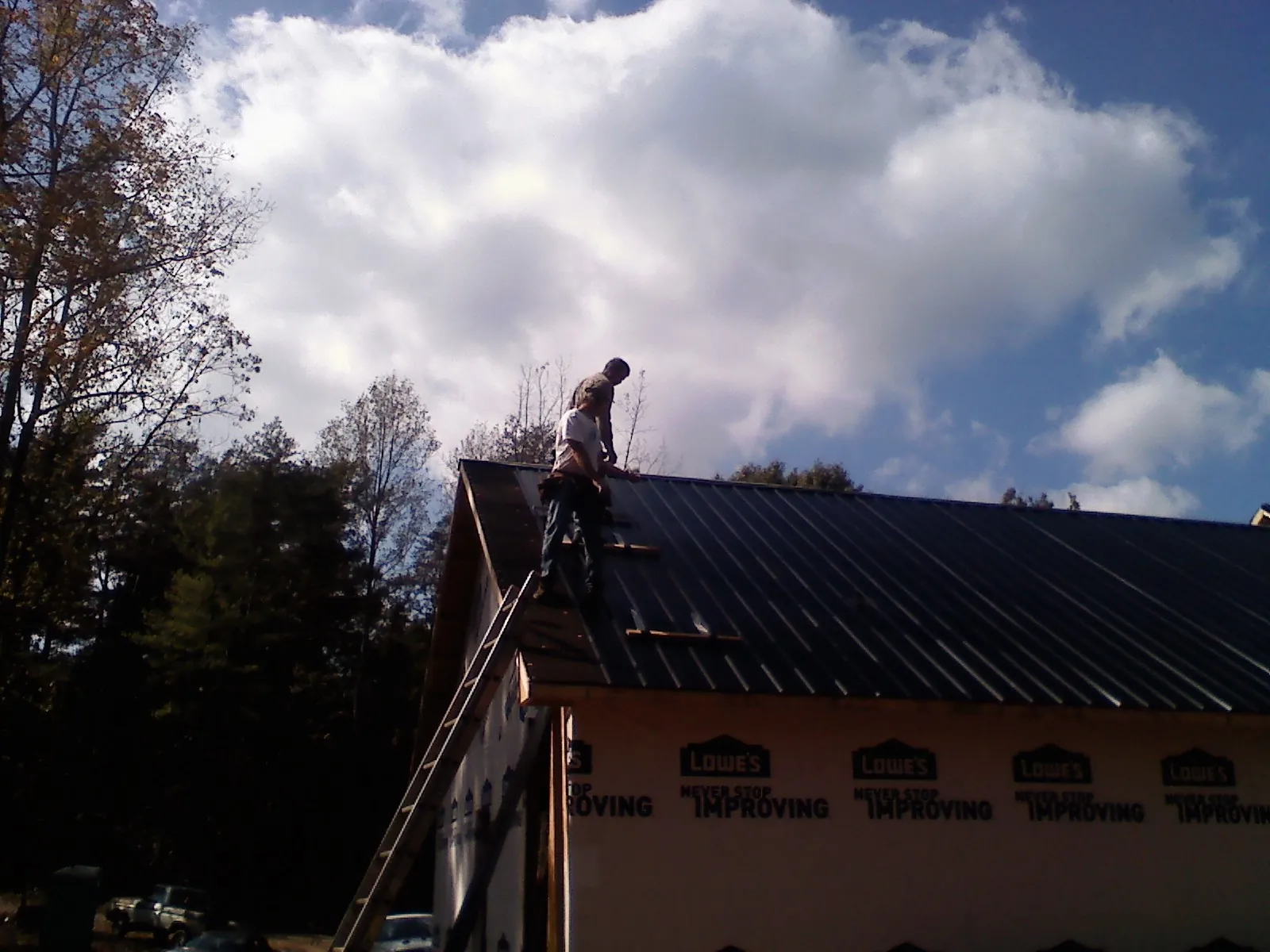 Roofer fastening dark metal panels high against a cloudy sky, from a Roof Inspection job in Rougemont