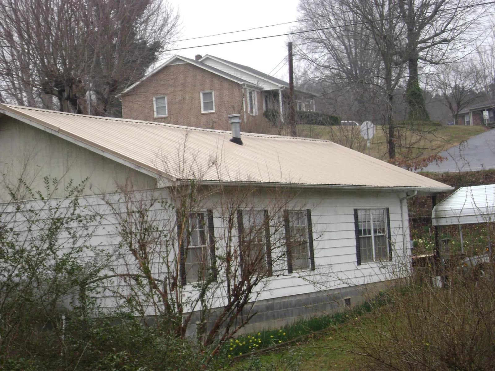 Tan metal roof on a white sided house set into a hillside — Commercial Roofing by Roofing Brothers in Rougemont