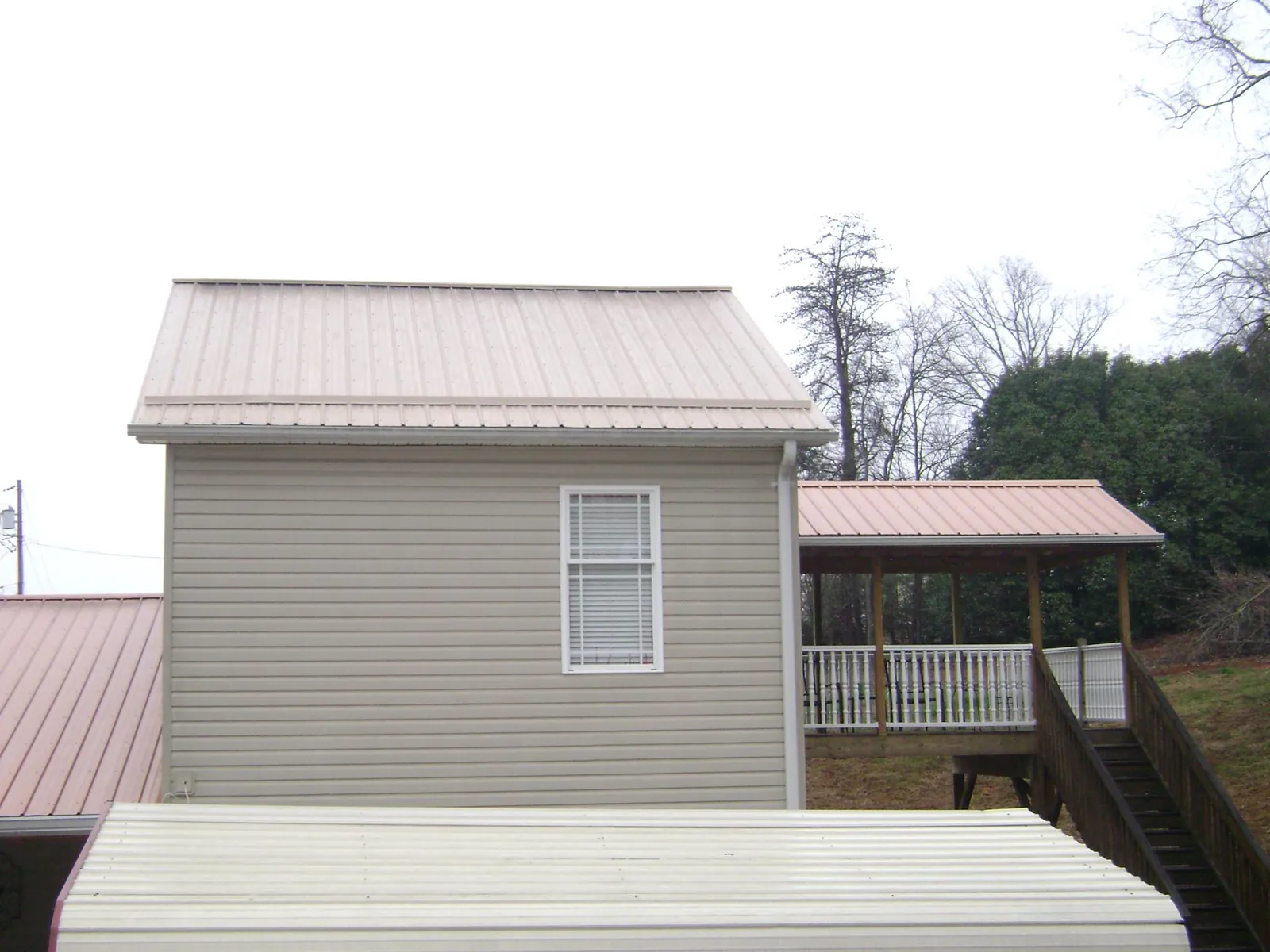Tan metal roofs on a two story addition and attached porch, from a Roof Replacement job in Rougemont